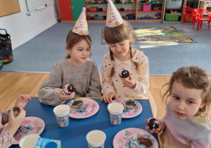 Grupa dzieci siedzi przy stole i spożywa słodkości