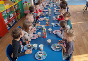 Dzieci siedzą przy stole i spożywają słodkości od Justyny i Marceliny