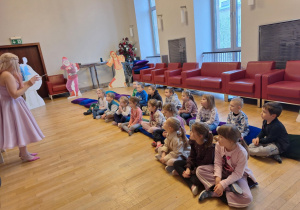 Dzieci siedzą na poduchach i słuchają pani prowadzącej