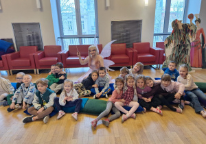 Dzieci siedzą na poduchach i pozują do zdjęcia z panią prowadzącą