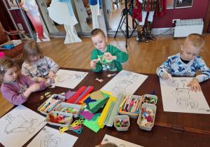 Grupa dzieci siedzi przu stole i wykonuje prace plastyczną