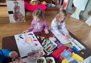 Grupa dzieci siedzi przu stole i wykonuje prace plastyczną