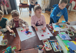 Grupa dzieci siedzi przu stole i wykonuje prace plastyczną