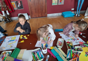 Grupa dzieci siedzi przu stole i wykonuje prace plastyczną