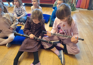 Dziewczynki siedzą na poduczach i oglądają instrument