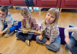 Dziewczynki siedzą na poduczach i oglądają instrument
