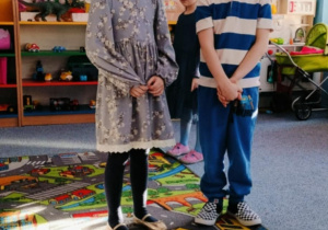 Dziewczynka i chłopiec stoją na dywanie i recytują wiersz