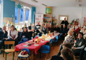 Babcie i Dziadkowie siedzą przy stołach i oglądają występy wnuków