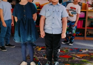 Dziewczynka i chłopiec stoją na dywanie i recytują wiersz