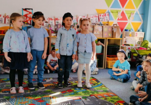 Grupa dzieci stoi na dywanie i recytuje wiersz