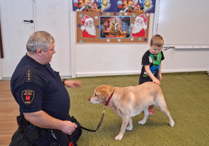 Dziecko głaszcze psa pod nadzorem strażnika