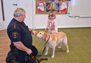 Dziecko głaszcze psa pod nadzorem strażnika