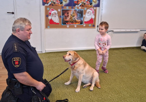 Dziecko głaszcze psa pod nadzorem strażnika