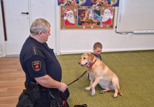 Dziecko głaszcze psa pod nadzorem strażnika