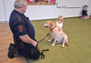 Dziecko głaszcze psa pod nadzorem strażnika