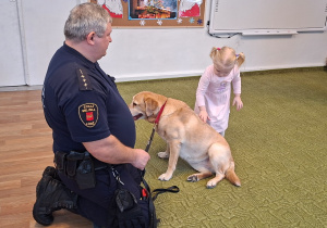 Dziecko głaszcze psa pod nadzorem strażnika