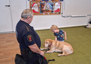 Dziecko głaszcze psa pod nadzorem strażnika