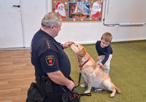 Dziecko głaszcze psa pod nadzorem strażnika