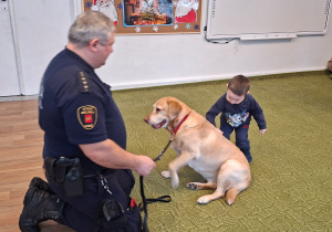 Dziecko głaszcze psa pod nadzorem strażnika