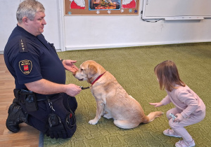 Dziecko głaszcze psa pod nadzorem strażnika