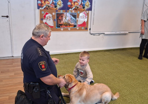 Dziecko głaszcze psa pod nadzorem strażnika