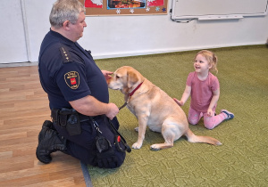 Dziecko głaszcze psa pod nadzorem strażnika