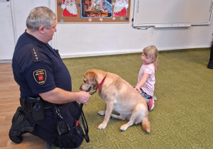 Dziecko głaszcze psa pod nadzorem strażnika