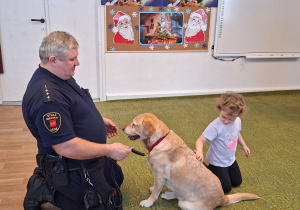 Dziecko głaszcze psa pod nadzorem strażnika