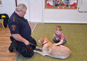 Dziecko głaszcze psa pod nadzorem strażnika
