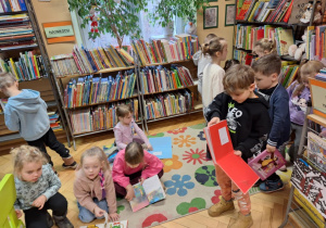 Grupa dzieci siedzi na dywanie i ogląda książki