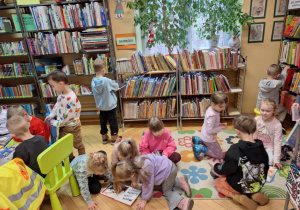 Grupa dzieci siedzi na dywanie i ogląda książki