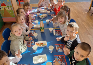 Grupa dzieci z Julkiem siedzą przy stole i spożywają słodkości