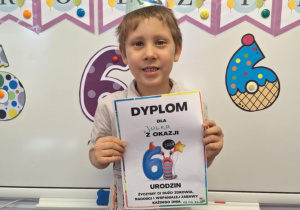 Julek stoi i pozuje do zdjęcia z dyplomem