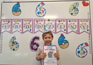 Julek siedzi na krześle i pozuje do zdjęcia z dyplomem