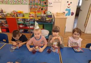 Dzieci siedzą przy stole i spożywają słodkości z solenizantem