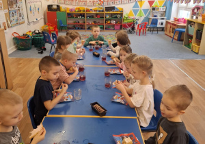 Dzieci siedzą przy stole i spożywają słodkości z solenizantem