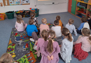 Dzieci siedzą na dywanie i oglądają prezentacje multimedialną- jak powsyała pizza