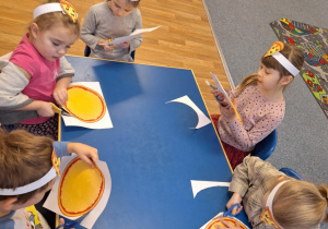 Grupa dzieci siedzą przy stole i wycinają kształt pizzy
