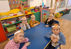 Grupa dzieci siedzi przy stole i pozuje do zdjęcia