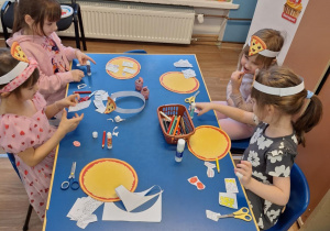 Grupa dzieci siedzi przy stole i wycina produkty do pizzy