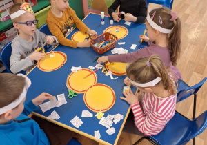 Grupa dzieci siedzi przy stole i wycina produkty do pizzy