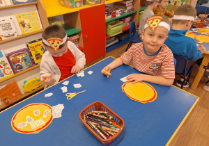 Grupa dzieci siedzi przy stole i wycina produkty do pizzy