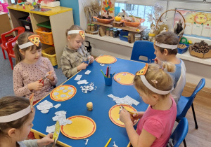 Grupa dzieci siedzi przy stole i wycina produkty do pizzy