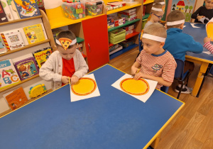 Grupa dzieci siedzi przy stole i wycina kształt pizzy