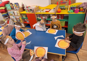 Grupa dzieci siedzi przy stole i wycina kształt pizzy