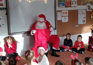 Dzieci siedzą przed Mikołajem, Mikołaj zagląda do worka
