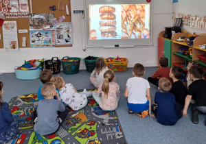 Dzieci siedzą na dywanie i oglądają prezentacje multimedialą-tłusty czwartek