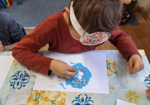 Chłopiec siedzi przy stole i wykonuje pracę plastyczną