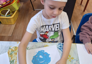 Chłopiec siedzi przy stole i wykonuje pracę plastyczną