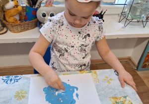 Dziewczynka siedzi przy stole i wykonuje pracę plastyczną